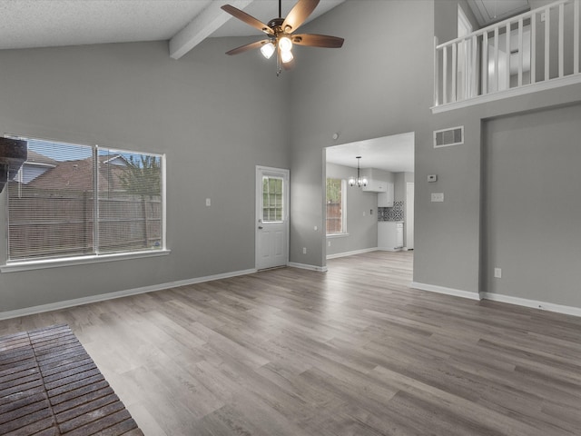 unfurnished living room with ceiling fan with notable chandelier, wood-type flooring, and high vaulted ceiling