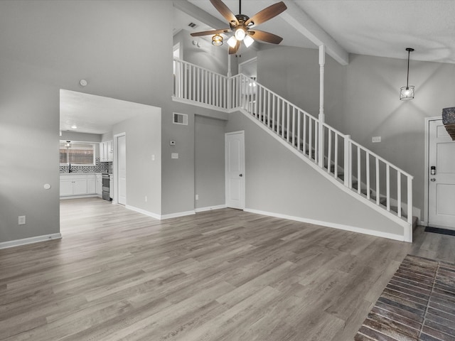 unfurnished living room featuring beam ceiling, light hardwood / wood-style floors, high vaulted ceiling, and ceiling fan