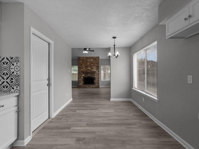 unfurnished dining area with a textured ceiling, ceiling fan with notable chandelier, light hardwood / wood-style floors, and a fireplace