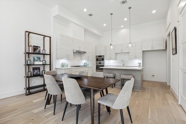 dining area with light hardwood / wood-style floors, sink, and a high ceiling