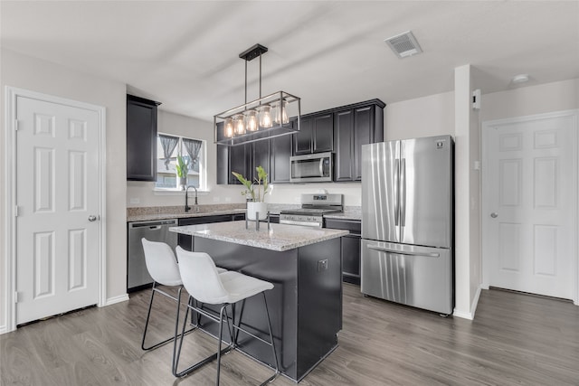 kitchen with a center island, light stone counters, pendant lighting, appliances with stainless steel finishes, and hardwood / wood-style flooring