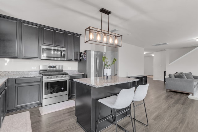 kitchen featuring pendant lighting, dark wood-type flooring, appliances with stainless steel finishes, a kitchen island, and a kitchen bar