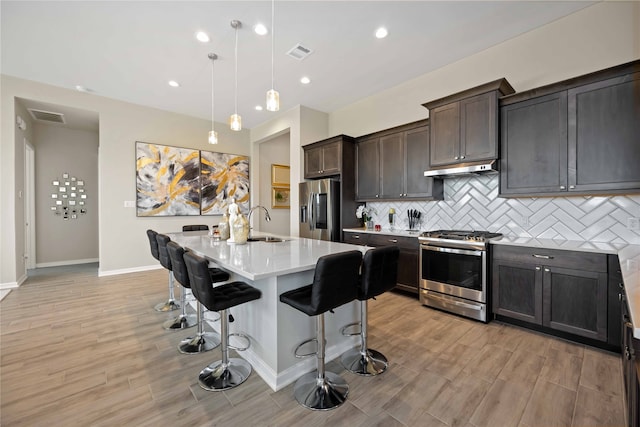 kitchen with a center island with sink, hanging light fixtures, appliances with stainless steel finishes, light hardwood / wood-style floors, and a kitchen bar