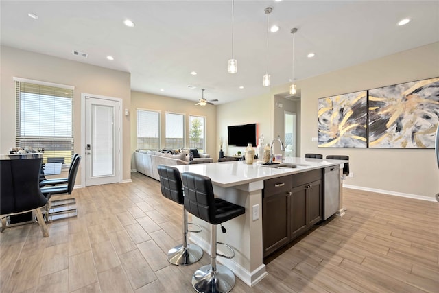 kitchen with ceiling fan, an island with sink, hanging light fixtures, and light hardwood / wood-style flooring