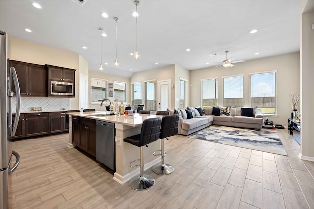 kitchen with a kitchen island with sink, sink, ceiling fan, light hardwood / wood-style floors, and stainless steel appliances