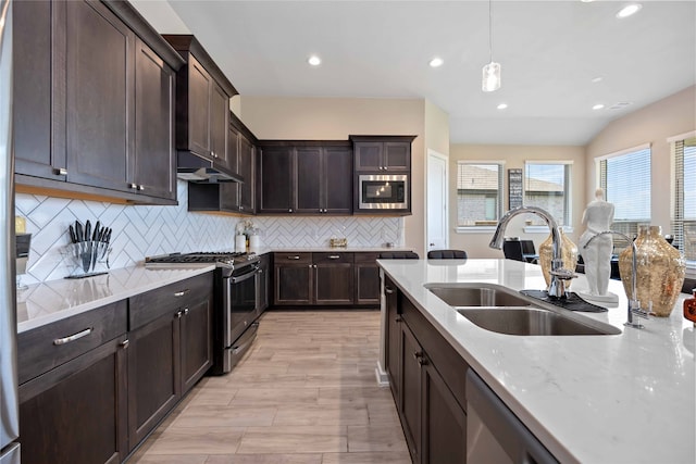 kitchen featuring appliances with stainless steel finishes, backsplash, sink, light hardwood / wood-style flooring, and hanging light fixtures