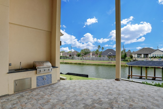 view of patio / terrace with grilling area, sink, a water view, and an outdoor kitchen