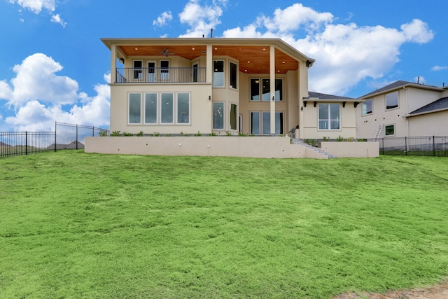 rear view of house featuring ceiling fan, a yard, and a balcony