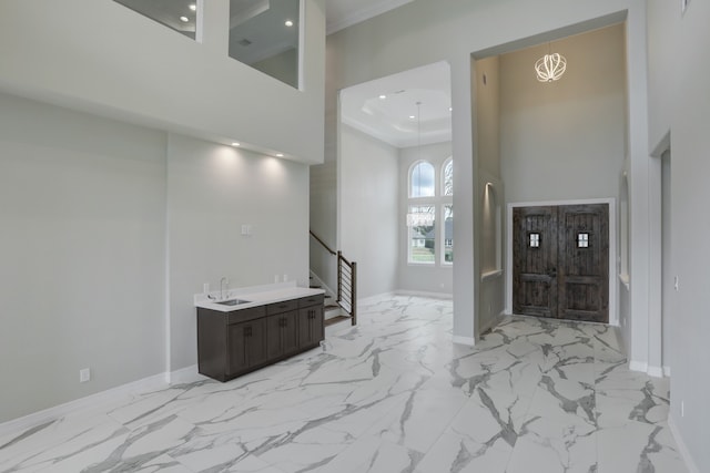 entrance foyer with a high ceiling, an inviting chandelier, crown molding, and sink