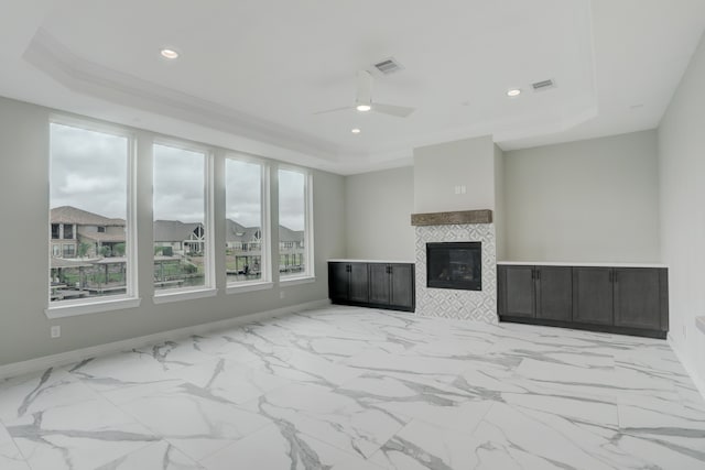 unfurnished living room with ceiling fan, a raised ceiling, crown molding, and a tiled fireplace