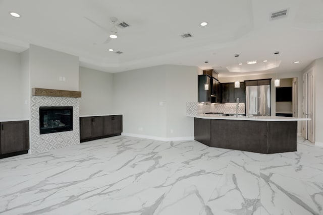 kitchen with a raised ceiling, a fireplace, decorative light fixtures, kitchen peninsula, and stainless steel refrigerator