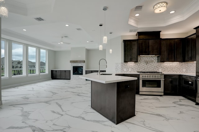 kitchen with ornamental molding, stainless steel range, a raised ceiling, hanging light fixtures, and an island with sink