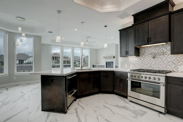 kitchen with decorative light fixtures, sink, high end stainless steel range oven, and a tray ceiling