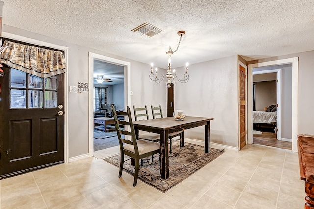 dining room featuring ceiling fan with notable chandelier, light tile patterned flooring, and a textured ceiling