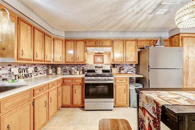 1215 Esther St, Kemah, TX 77565 - kitchen featuring stainless steel gas stove, freestanding refrigerator, under cabinet range hood, light countertops, and a textured ceiling