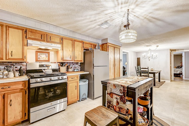 1215 Esther St, Kemah, TX 77565 - kitchen featuring stainless steel gas stove, under cabinet range hood, freestanding refrigerator, a chandelier, and light countertops