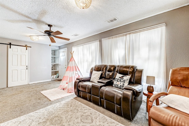 living room featuring a barn door, ceiling fan, light colored carpet, and a textured ceiling