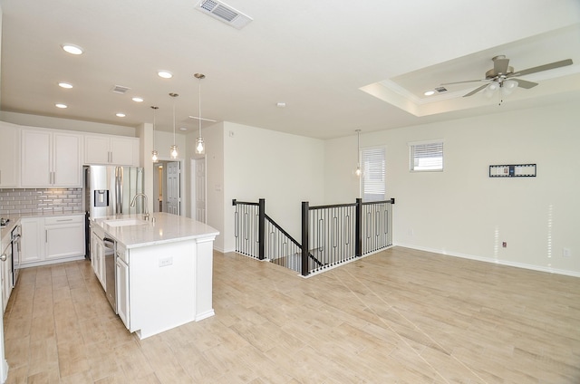 kitchen featuring sink, decorative light fixtures, a center island with sink, white cabinets, and light wood-type flooring