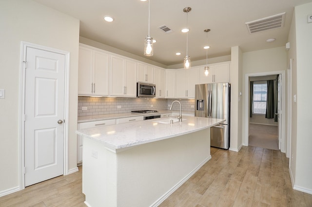 kitchen with a center island with sink, white cabinets, sink, light wood-type flooring, and stainless steel appliances