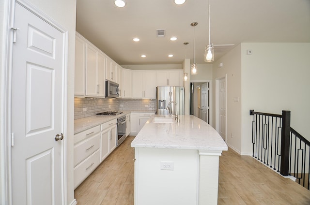 kitchen with a center island with sink, hanging light fixtures, sink, appliances with stainless steel finishes, and white cabinetry