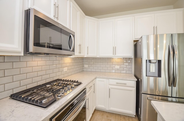 kitchen featuring white cabinets, appliances with stainless steel finishes, tasteful backsplash, and light stone countertops