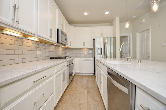 kitchen featuring light stone countertops, appliances with stainless steel finishes, white cabinetry, and sink