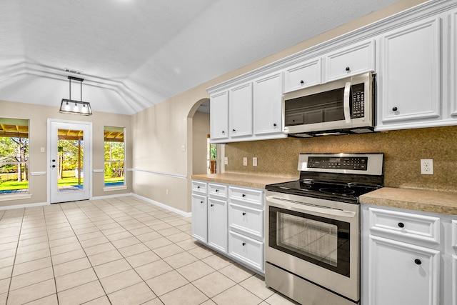 kitchen with lofted ceiling, white cabinets, light tile patterned floors, appliances with stainless steel finishes, and tasteful backsplash