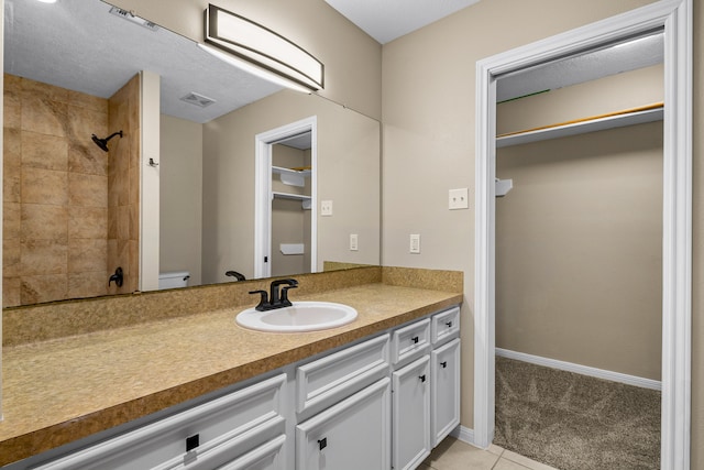 bathroom featuring a tile shower, vanity, a textured ceiling, tile patterned flooring, and toilet