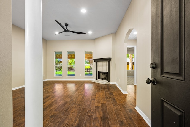 unfurnished living room with ceiling fan, a fireplace, and dark wood-type flooring