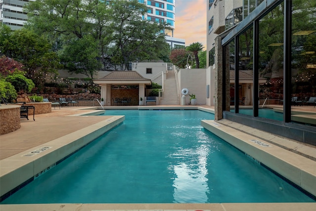 pool at dusk featuring a gazebo and a patio