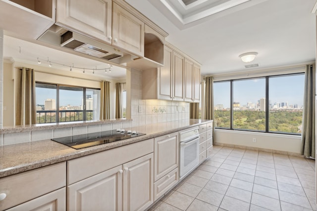 kitchen with backsplash, black electric stovetop, oven, light tile patterned floors, and light stone counters