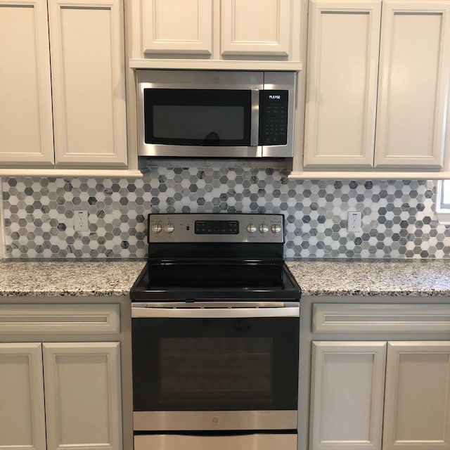 kitchen featuring white cabinetry, decorative backsplash, light stone countertops, and appliances with stainless steel finishes