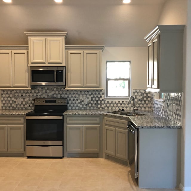 kitchen with gray cabinetry, dark stone counters, sink, tasteful backsplash, and stainless steel appliances