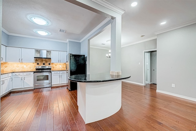 kitchen with hardwood / wood-style floors, white cabinets, wall chimney range hood, and appliances with stainless steel finishes