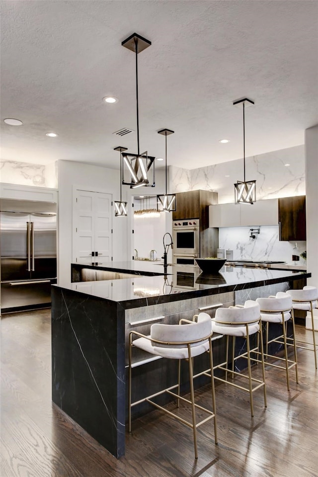 kitchen featuring pendant lighting, stainless steel double oven, dark wood-type flooring, and a breakfast bar area