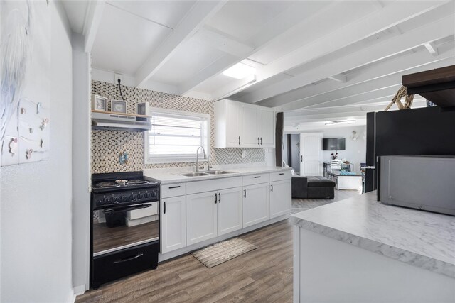 219 Fort Velasco Dr, Surfside Beach, TX 77541 - kitchen with a sink, black gas range, under cabinet range hood, wood finished floors, and tasteful backsplash