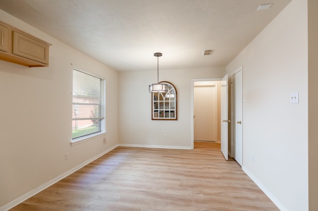 unfurnished dining area with light hardwood / wood-style floors and a textured ceiling