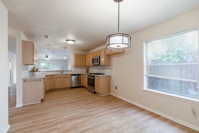 kitchen with kitchen peninsula, appliances with stainless steel finishes, light brown cabinets, pendant lighting, and light hardwood / wood-style floors