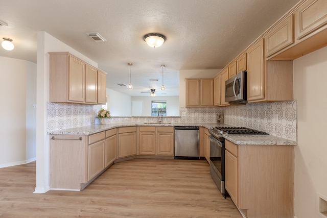 kitchen featuring sink, stainless steel appliances, decorative light fixtures, light brown cabinetry, and light wood-type flooring