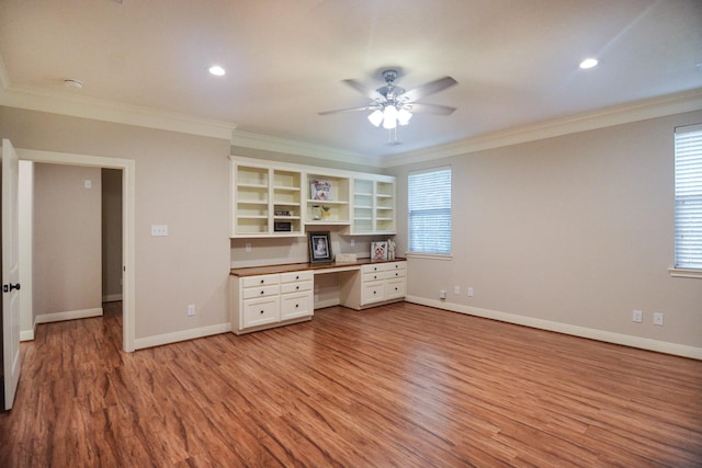 unfurnished office with ceiling fan, light hardwood / wood-style flooring, built in desk, and ornamental molding