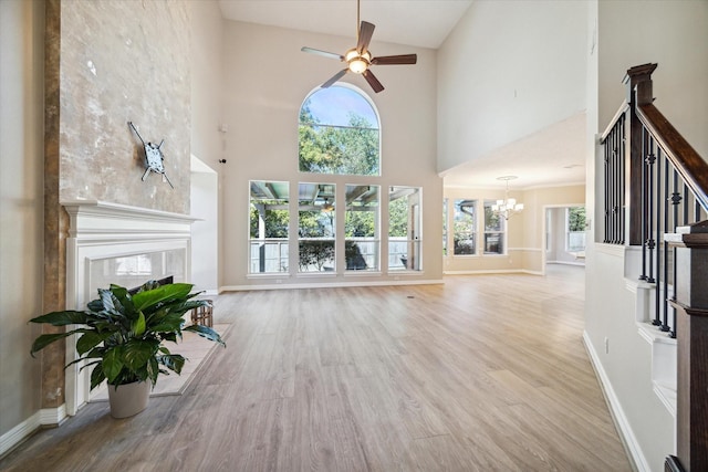 unfurnished living room with a tile fireplace, ceiling fan with notable chandelier, a high ceiling, and light wood-type flooring