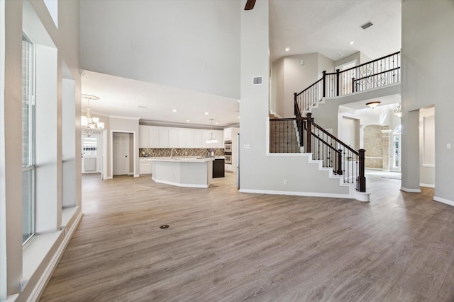 unfurnished living room with plenty of natural light, sink, light hardwood / wood-style floors, and a notable chandelier