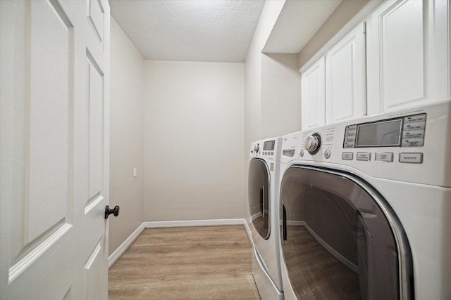 laundry room featuring cabinets, washer and dryer, a textured ceiling, and light wood-type flooring