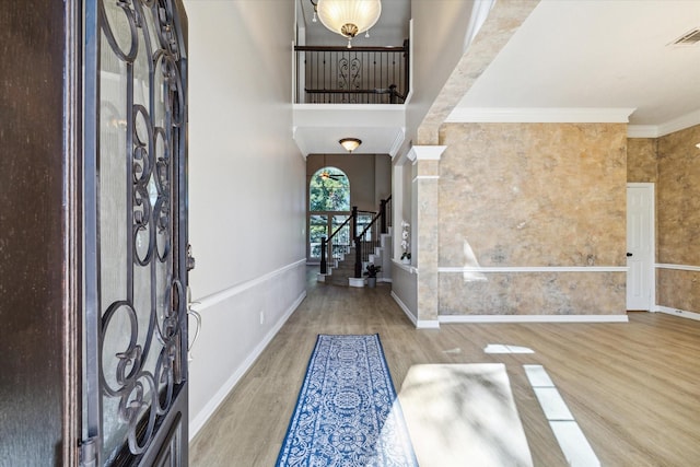 entrance foyer featuring a towering ceiling, wood-type flooring, ornamental molding, and decorative columns