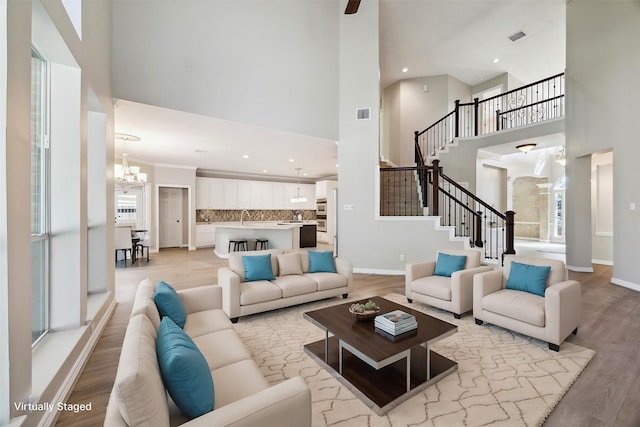 living room with sink, a high ceiling, a chandelier, and light wood-type flooring