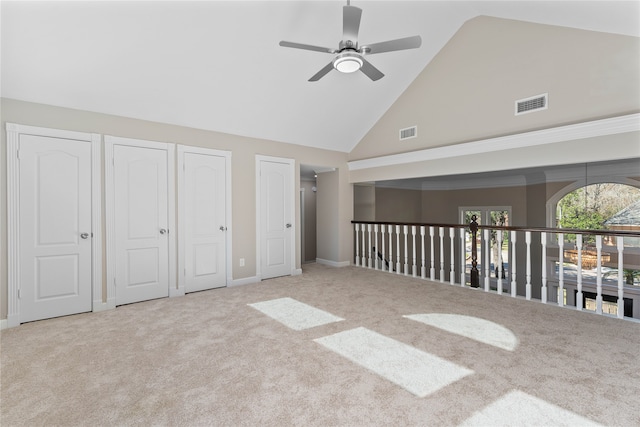 unfurnished bedroom featuring light carpet, high vaulted ceiling, ceiling fan, and multiple closets