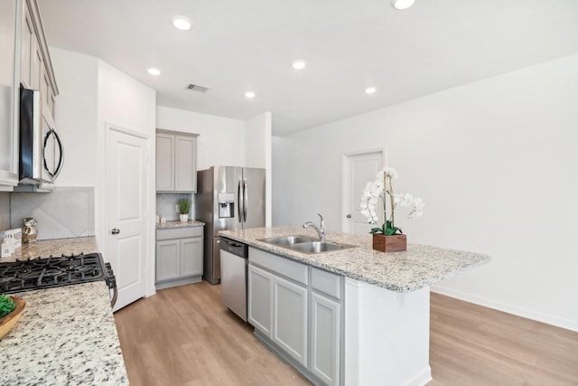 kitchen featuring sink, appliances with stainless steel finishes, light stone countertops, a kitchen island with sink, and backsplash