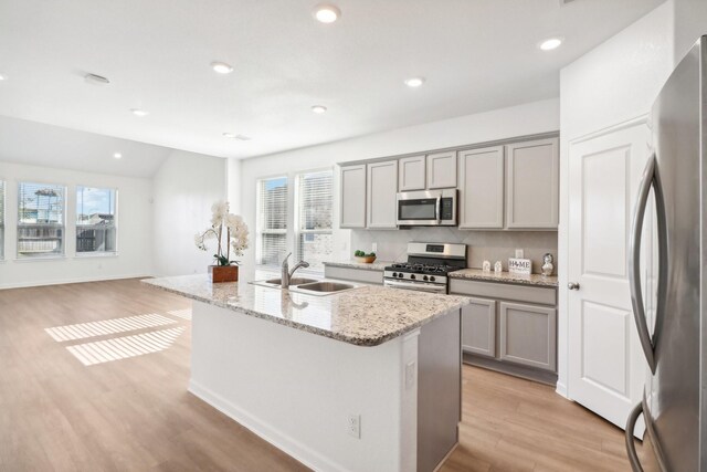 kitchen with sink, gray cabinets, light stone countertops, an island with sink, and appliances with stainless steel finishes