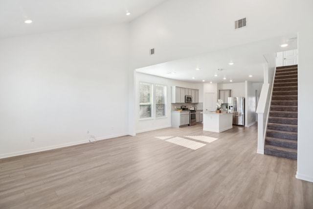 unfurnished living room featuring a towering ceiling and light hardwood / wood-style floors