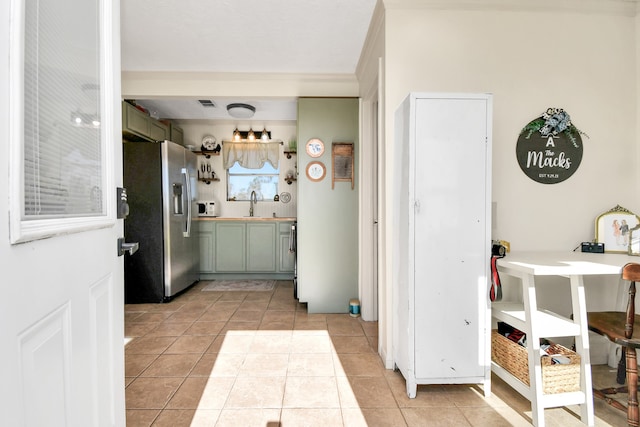 kitchen with stainless steel refrigerator with ice dispenser, light tile patterned floors, green cabinetry, and sink